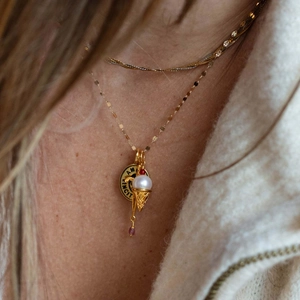 Detail of gold layered necklace with engraved Amor Vincit disk and pearl ice cream pendant