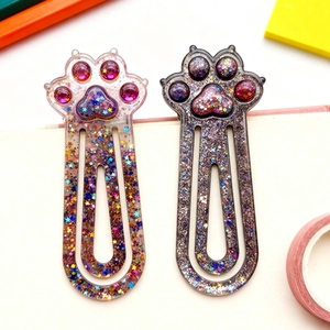 Glittery cat paw resin bookmark clips with colorful sequins and stars on a notebook