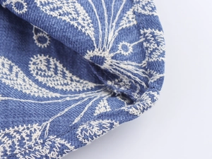 Détail du tissu bleu de la robe chemise avec des broderies florales blanches complexes