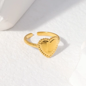 Detail shot of a gold heart-shaped open ring with beaded edges on a white textured backdrop