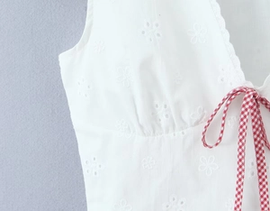 Close-up of white eyelet lace fabric featuring red and white checkered drawstrings