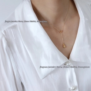 Close-up of minimalist gold teardrop pendant on Y-shaped necklace worn with a white shirt