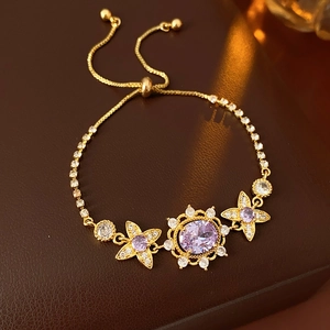 Close-up of a gold sunflower bracelet with purple gemstones on a leather background