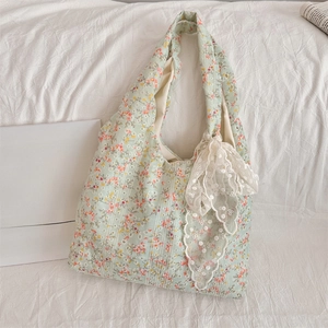 Detail of light green floral canvas tote bag featuring a large white lace bow accent