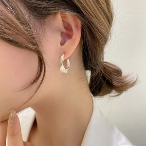 Close-up of elegant twisted white resin earrings with gold metal edges on model