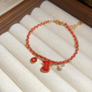 Detail showing red woven rope bracelet with gold lucky bag pendant and small diamond inlay