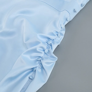 Detailed close-up of light blue satin dress with fabric buttons and side gathering detail
