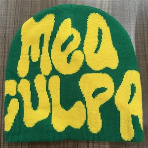 Detail shot of a green Mea Culpa knit beanie with yellow lettering on wood background