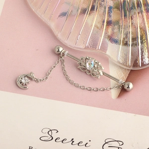 Detail of industrial barbell ear piercing with opal lotus and moon star dangle chain