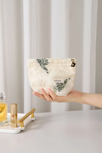 Detail of embroidered floral cotton linen makeup bag held in hand with accessories