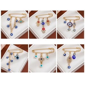 Detailed views of gold-plated evil eye and hamsa hand safety pin brooches with crystals