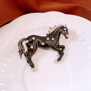 Detail of vintage enamel horse brooch with sparkling rhinestones on ceramic dish