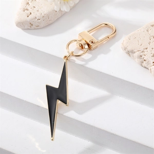 Detail of lightning bolt keychain with black enamel and gold finish on stone surface