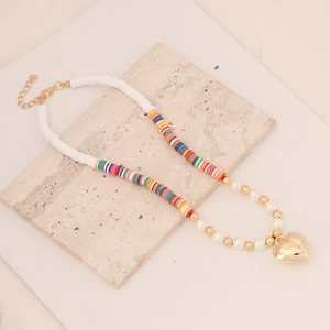 Detail of bohemian polymer clay necklace with pearls and gold heart pendant on marble