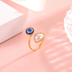 Detail of adjustable gold-plated ring with blue evil eye bead and heart pearl on pink background
