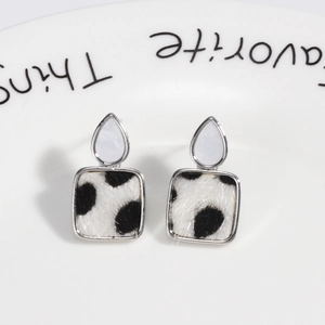 Macro shot of silver geometric square earrings with black and white cow print fur texture