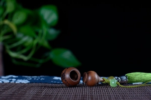 Carved sandalwood sachet pendant with green silk tassels and jade beads on black background