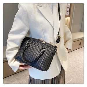 Détail d'un sac à main noir tressé avec ferrures dorées porté sur une veste en tweed