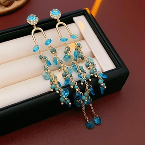 Detailed macro of gold drop earrings with blue crystal beads and cascading long tassels