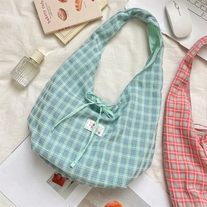 Detail of light blue checkered canvas tote bag with drawstring bow and small logo