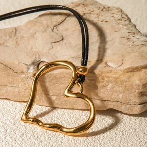 Macro shot of gold heart pendant on black cord necklace resting on a stone surface