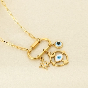 Detail of gold paperclip chain necklace with evil eye and star charms on beige fabric