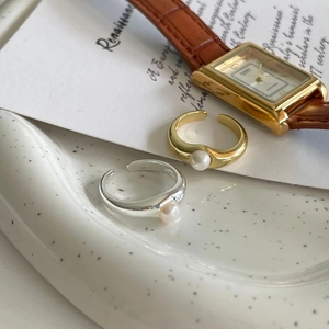 Detail of adjustable gold and silver pearl rings on a decorative ceramic plate