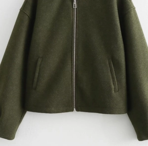 Detail of olive green bomber jacket featuring silver metal zipper and knit texture
