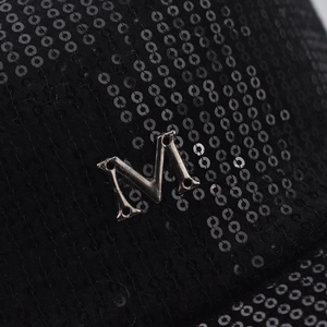 Gros plan détaillé de paillettes noires avec un logo M métallique argenté sur la casquette