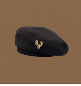 Detail of a black wool beret featuring a vintage gold heart-shaped metal buckle
