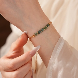 Détail du bracelet chaîne vintage doré avec pierres vertes carrées sur le poignet d'un mannequin