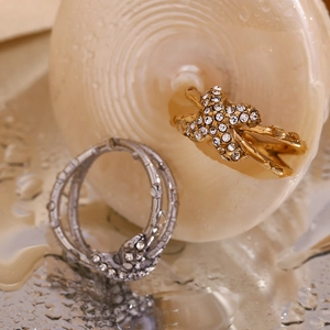 Detail von 18K Gold und Silber X-Ohrringen mit Zirkon-Mikro-Inlay auf Wasseroberfläche