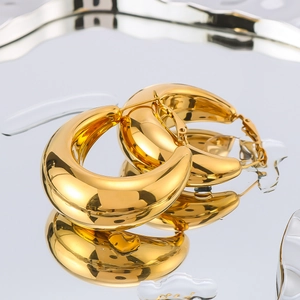Minimalist gold hollow hoop earrings with polished finish on a reflective water surface