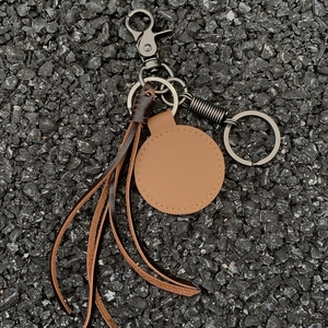 Handmade woven leather keychain with brown fringe and dark nickel clasp on stone surface