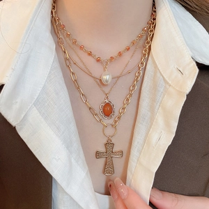 Close-up of layered gold cross necklace with acrylic pearls and red gemstone pendants