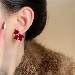 Detail of red flocked pony earring with golden bow on female model in winter fur coat