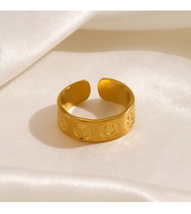 Close-up of gold-plated smiley face ring on white silk, showing geometric wide band texture