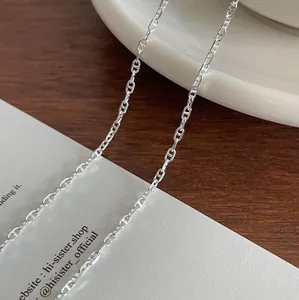 Detail of minimalist silver anchor chain anklet on a white plate and wooden desk
