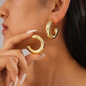 Close-up of thick gold-plated C-shaped hoop earrings with a smooth metallic finish
