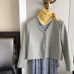 Close-up of a light green short blazer and yellow plaid neck scarf on a metal hanger