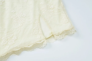 Detail of off-white lace dress featuring a side slit and intricate scalloped lace edges