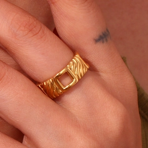 Close-up of a gold square cutout ring with textured diagonal patterns on the finger