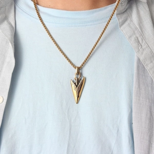 Close-up of golden arrowhead pendant with textured design on a stylish box chain