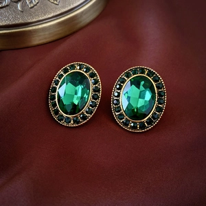 Macro shot of vintage emerald oval studs with gold-tone borders on dark red silk