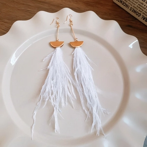 Detail of long white feather tassel earrings with gold metal top on a white ceramic plate