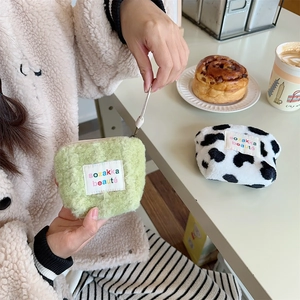 Mini plush makeup pouch in green and cow print showing fuzzy texture and drawstring closure