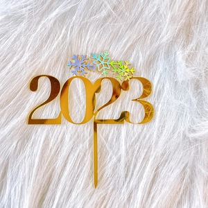 Detail of mirror gold acrylic 2023 cake topper with iridescent snowflake accents