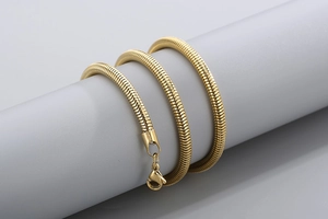 Détail d'un collier chaîne serpent dorée avec fermoir mousqueton sur un support gris