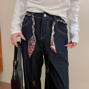 Close-up of printed silk scarf belt with wooden beads on high-waist dark blue jeans