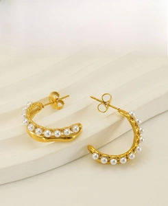 Détail de boucles d'oreilles créoles dorées en C avec perles blanches sur support blanc